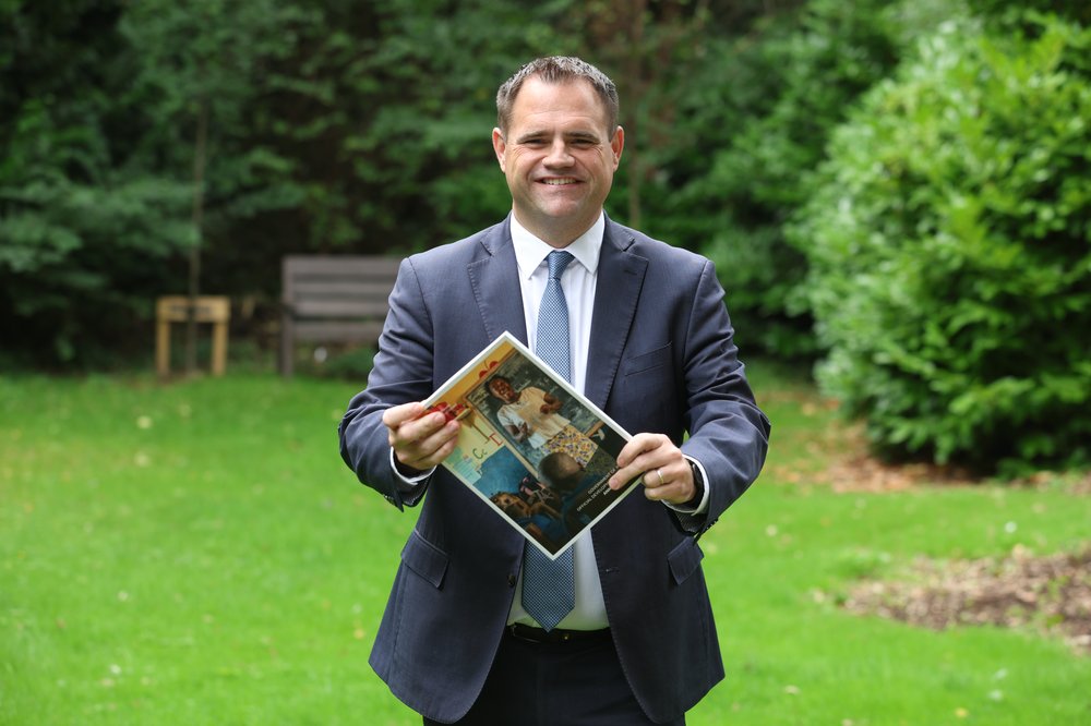 Minister Richmond holding the 2025 Irish Aid Annual Report in the gardens of Iveagh House.