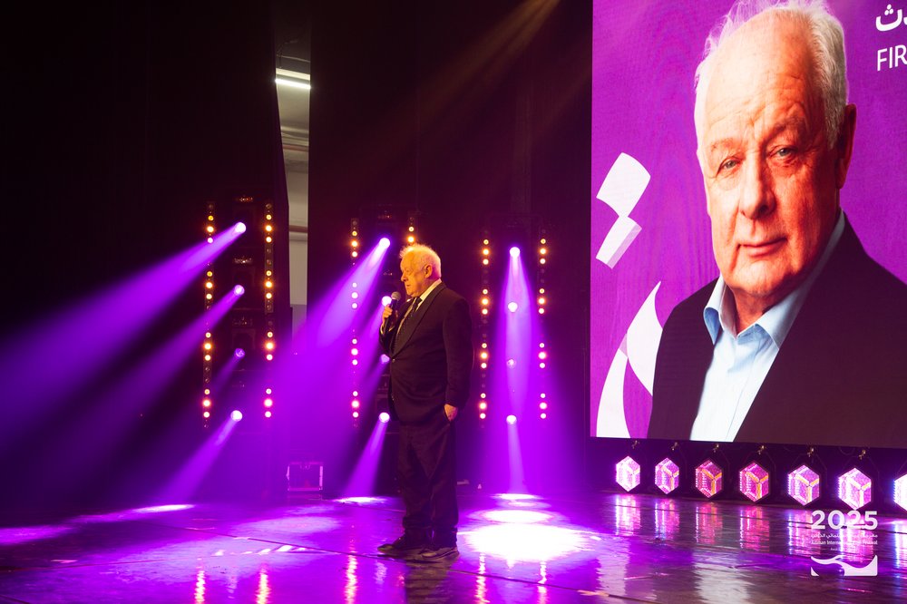 Jim Sheridan stands on a stage with his headshot behind him