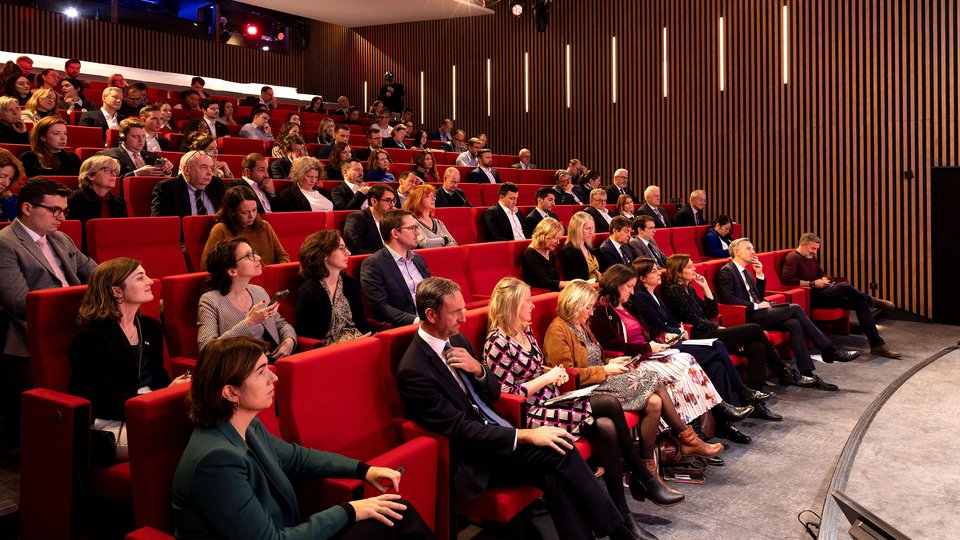 Crowd sitting in red stalls looking at a stage