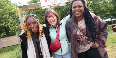 three women with their arms around each other in front of a wooden sign with Africa Day