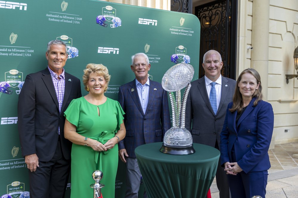 Mike Buddie, Ambassador Byrne Nason, John Anthony, Rick Steinbacher, and Susan Fox pose in front of green ESPN Embassy backdrop with Waterford Crystal trophy
