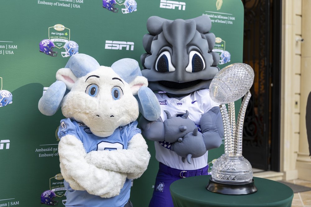 UNC mascot Ramses Jr. and TCU mascot SuperFrog pose with Waterford Crystal trophy in front of green Embassy and
