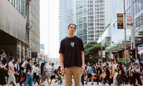 Chris Wong standing in the middle of a busy road with many people crossing the street behind him