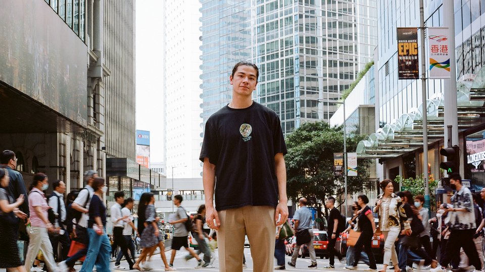 Chris Wong standing in the middle of a busy road with many people crossing the street behind him
