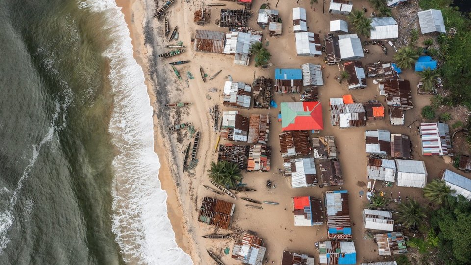 Looking down from above at a shoreline town in Liberia, waves crashing up on the shore