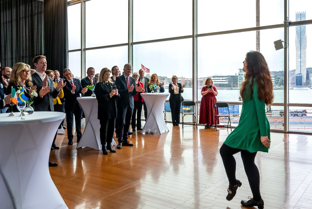A girl in a green dress performs an Irish dance in front of a cheering audience.