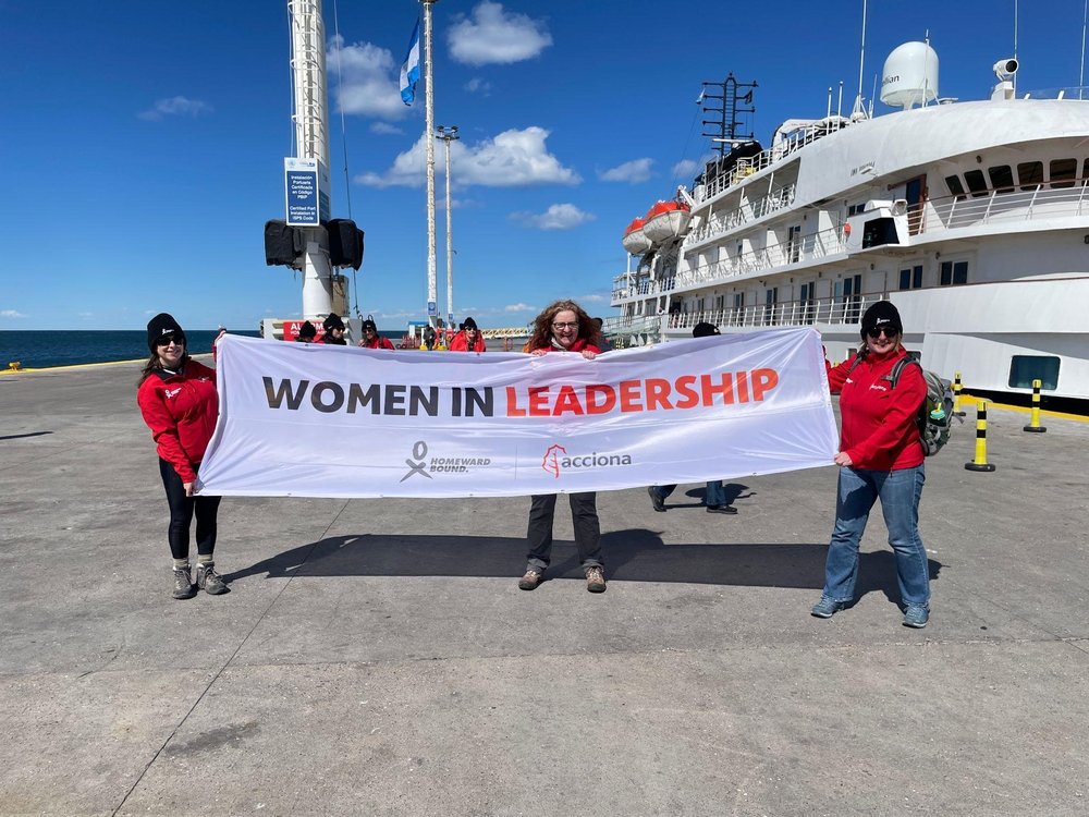 Niamh holds a Homeward Bound/Acciona Women in Leadership banner on the ship’s docks with two other members of the crew.