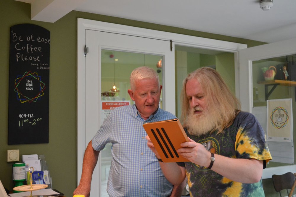 A younger man helping an older man with his tablet device.