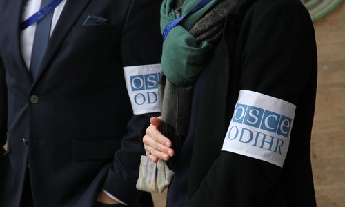 A woman and man wearing armbands with the OSCE logo.