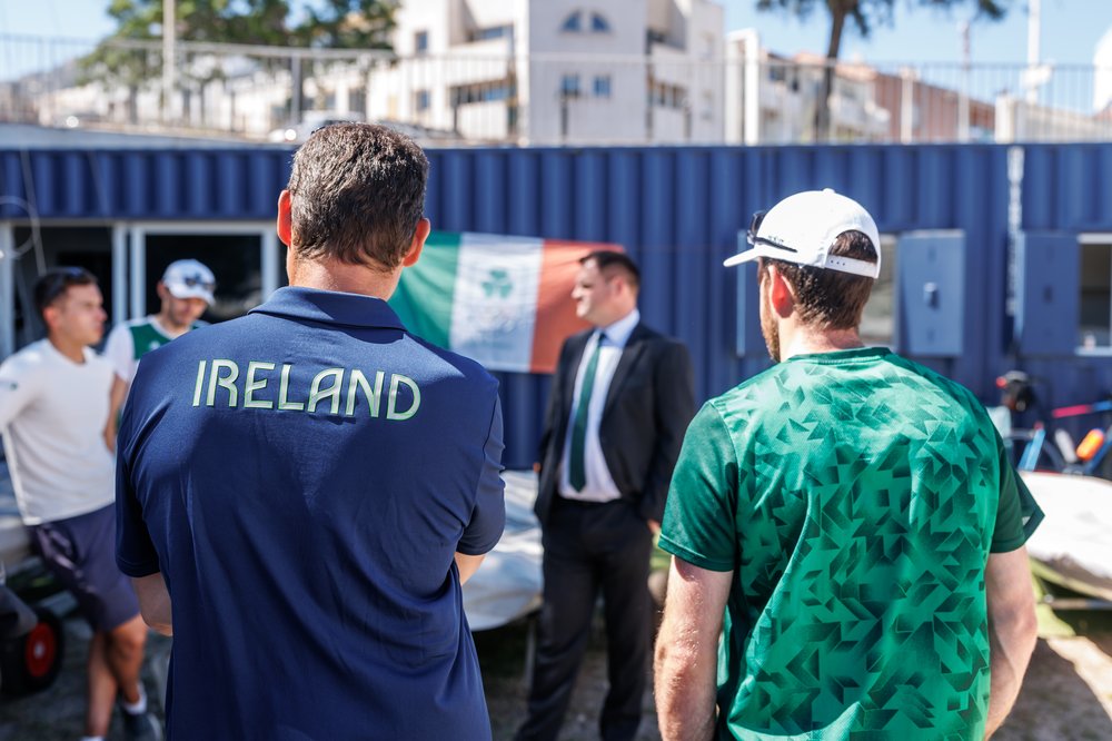 Deux voiliers de l'équipe d'Irlande tournent le dos à la caméra pendant que le ministre Richmond s'exprime.