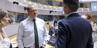 Minister Byrne stands in the Council meeting room speaking to his Dutch counterpart. They stand facing each other. The meeting room and interpretation boxes are visible in the background.