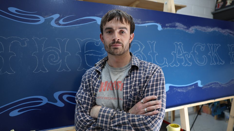 Lockie standing in front of an in progress handpainted sign