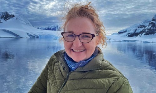 Wearing a puffy coat, Dr. Niamh Shaw smiles against a backdrop of mountains, snow and ice