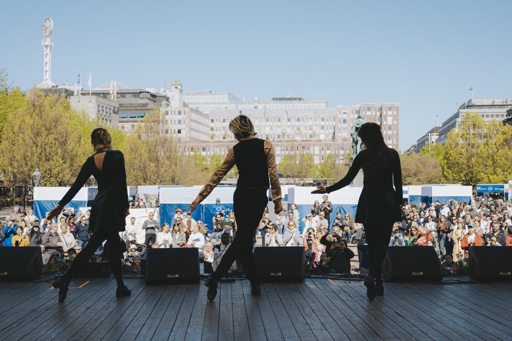 The silhouette of three Irish dance performers in front of a large crowd at Kungsträdgården in Stockholm.