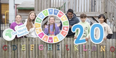 Children standing in front of a fence holding colour wheel featuring sustainable development goals