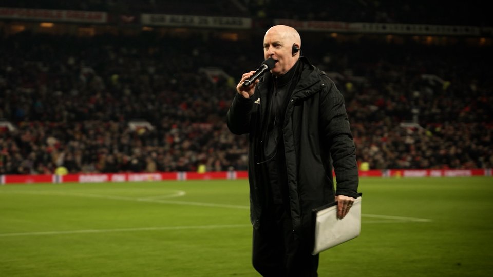 Man speaking into a mic on a football pitch