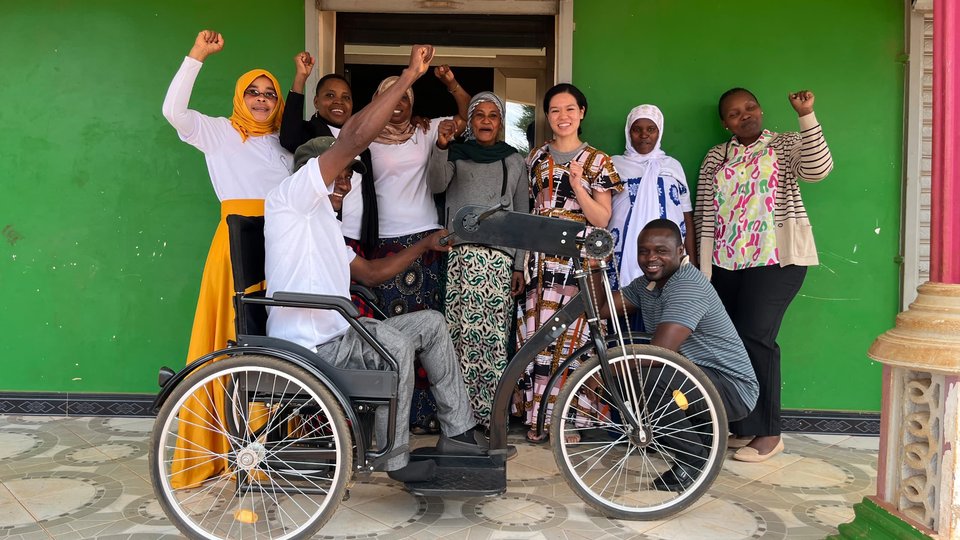 A group of people celebrating outside a doorway, with a man on a tricycle in front