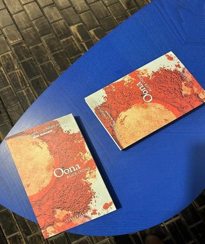 Two books by the author Alice Lyons lying on a blue table.