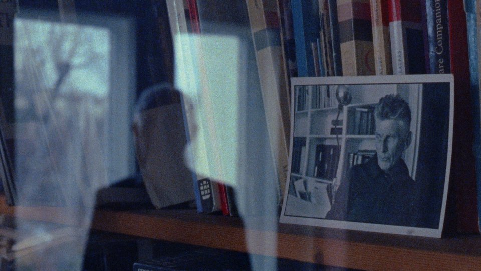 A photograph of Samuel Beckett rests on a bookshelf behind a glass door