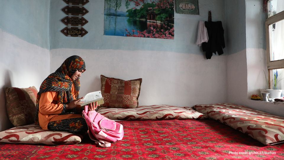 A girl sits on a cushion reading a book.