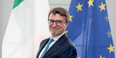 Ambassador Luke Feeney standing in front of Irish and EU flags