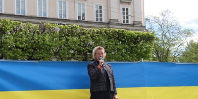 Ambassador Jones standing in front of a large Ukrainian flag giving remarks.