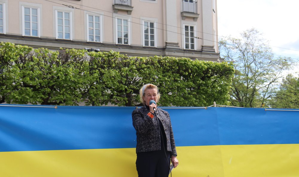 Ambassador Jones stands in front of a Ukrainian flag giving remarks.