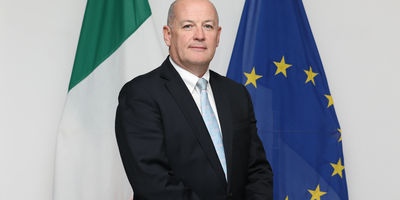 Ambassador Peter Ryan standing in front of the Irish and EU flags.