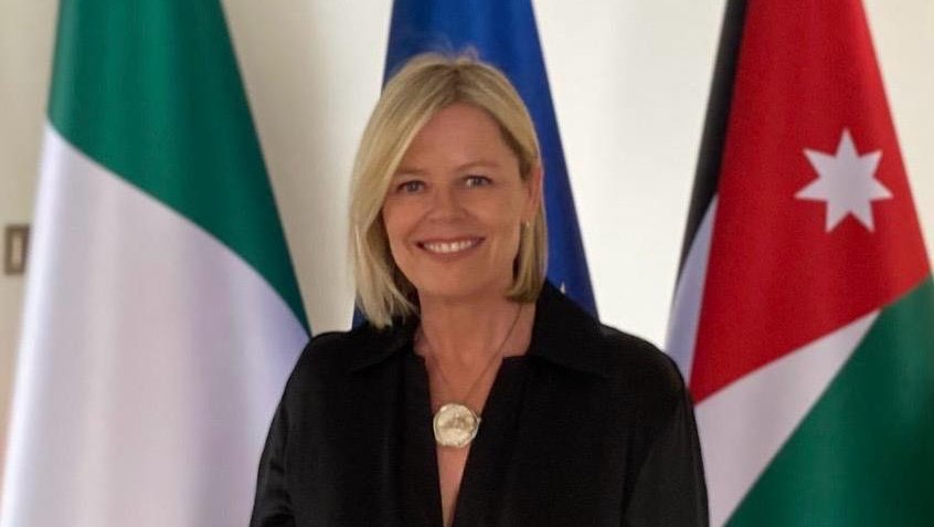 A woman wearing a black shirt standing in front of Irish and EU flags.