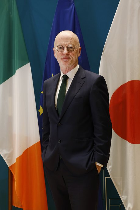 Man in a suit in front of Irish and Japanese national flags