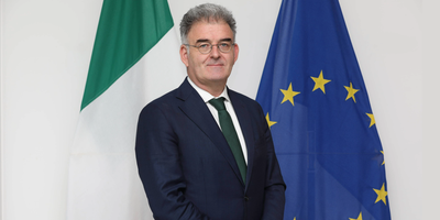 Ambassador Gerard Consindine standing in front of the Irish and EU flags.