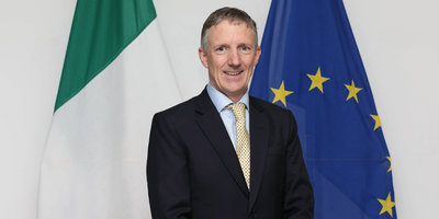 Headshot of Gerry Cunningham in front of the Irish and EU flags.