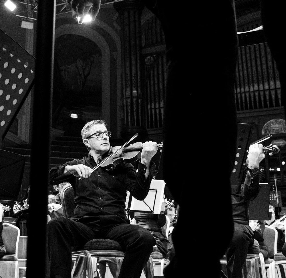 A man plays a violin as part of an orchestral concert