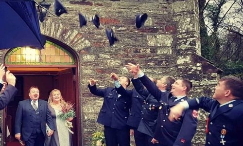People throwing their hats in the air as newlyweds walk out of a house