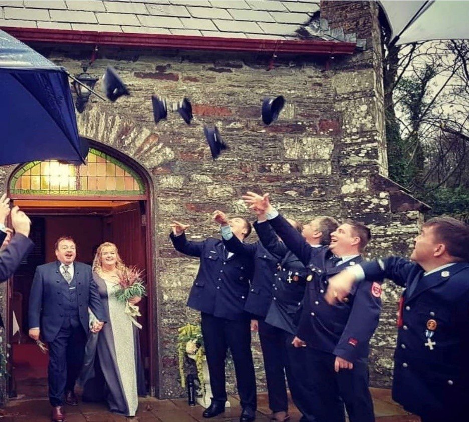 People throwing their hats in the air as newlyweds walk out of a house