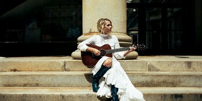 Aoife O'Donovan playing the guitar sitting on steps