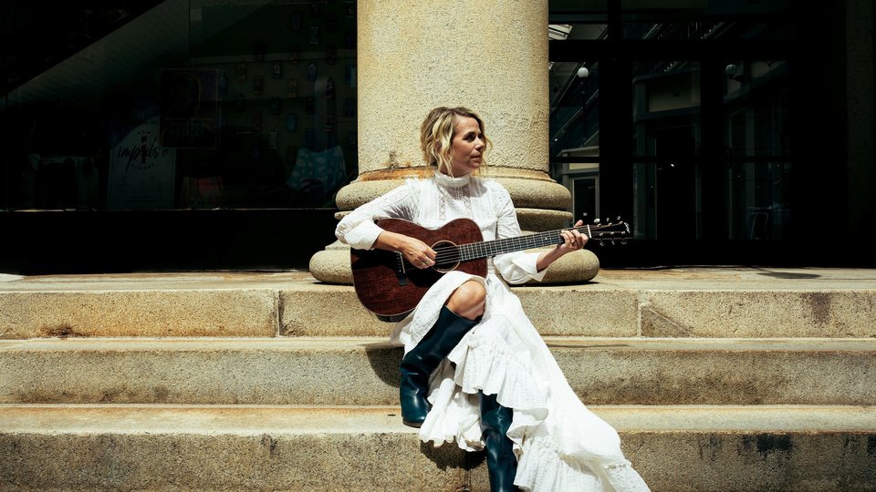 Aoife O'Donovan playing the guitar sitting on steps
