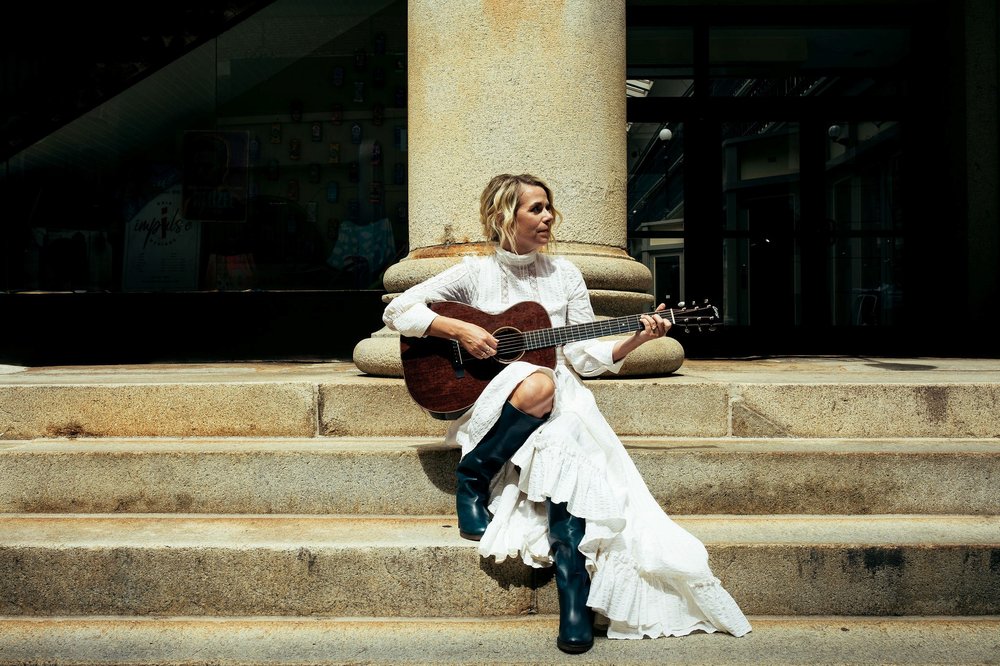 Aoife O'Donovan playing the guitar sitting on steps