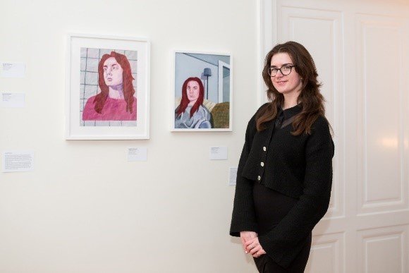 Artist standing beside her paintings hanging on a wall