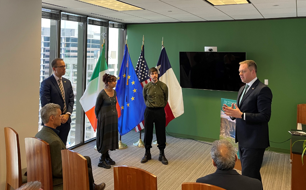four people standing presenting to a room with flags behind them