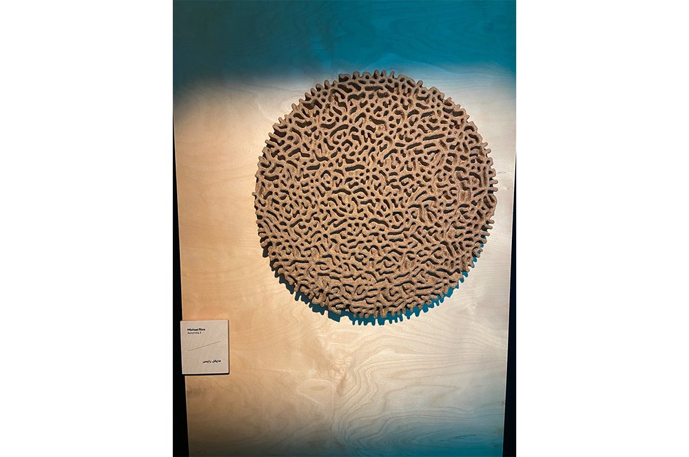 A circular maze-like flat scuplture displayed on a wall.