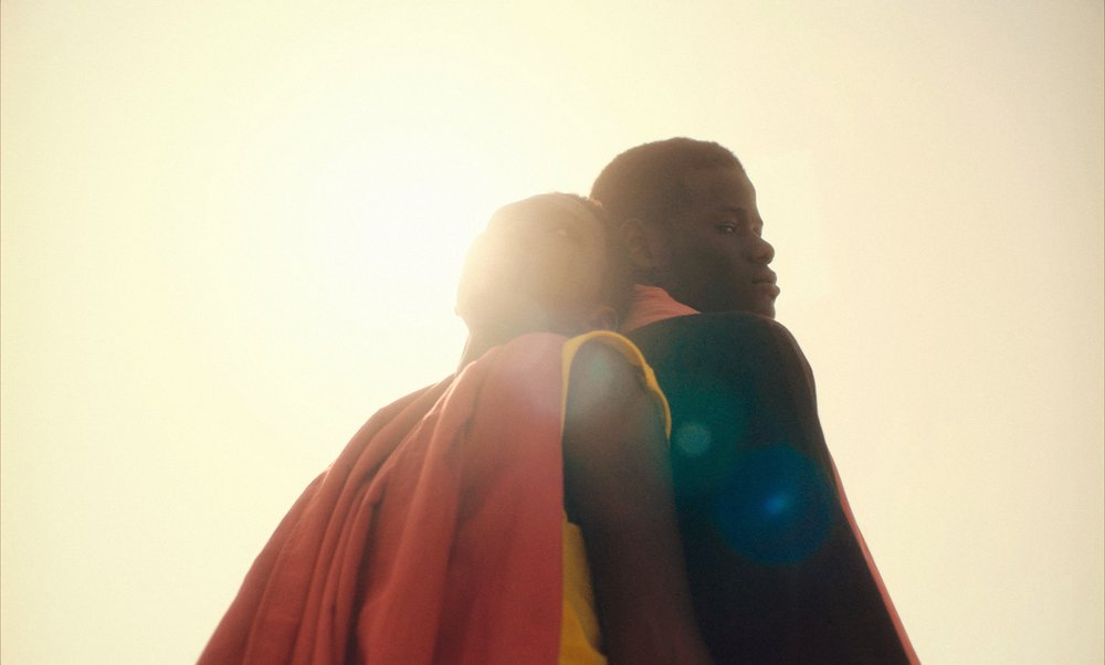Two people leaning on each other back to back in the bright sun.