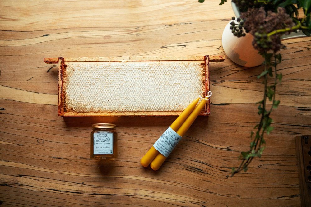 A raw honeycomb, a jar of honey, and beeswax taper candles