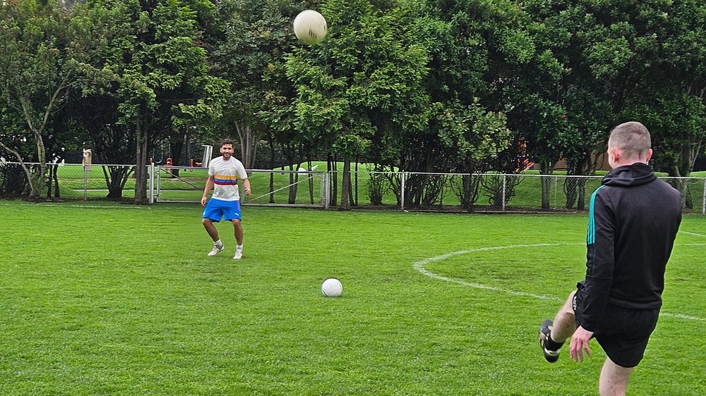 Two members of Bogotá Beithígh at a training session. They are kicking a ball to each other and it is mid-air.