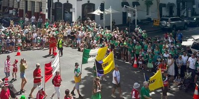 A crowd of people marching in Brisbane's Irish festival carrying county flags with a large group of onlookers