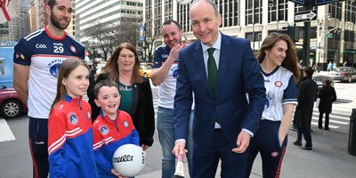 Children with a Gaelic football interacting with the Tánaiste who is holding a hurl, outside the Consulate building.