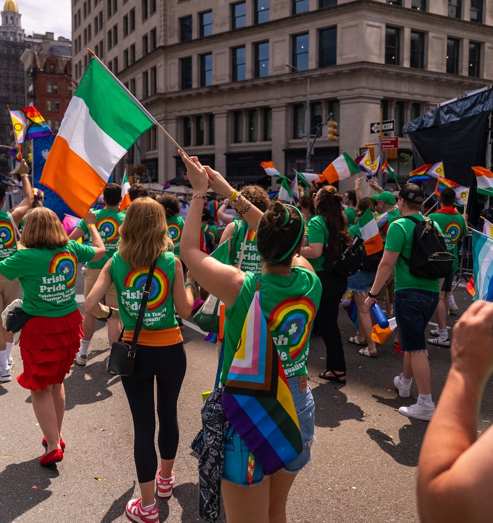 The back of the crowd at NYC Pride, a woman is waving an Irish flag