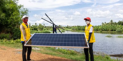 Two people carrying a large solar panel