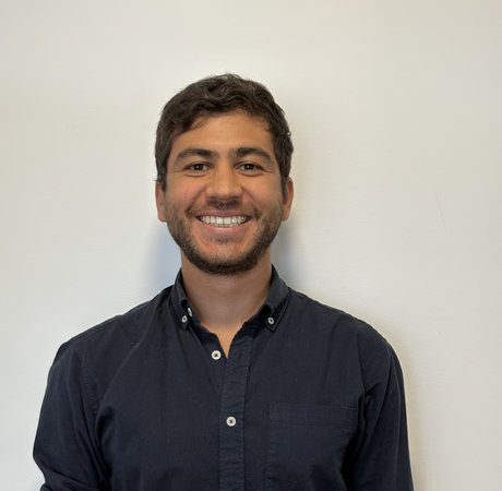 A headshot of Camilo smiling at the camera in a dark shirt.