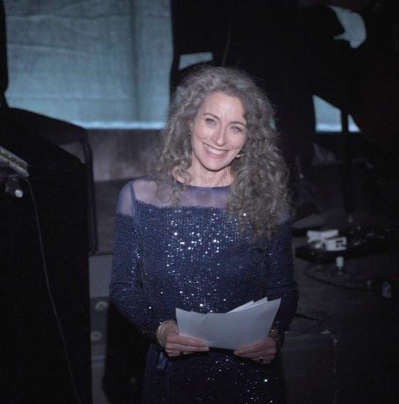 woman actress smiling, lit up on stage reading a poem, holding the text in front of her